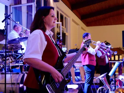 Musikerin am E-Bass, dahinter Schlagzeug und Trompeten